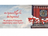 Po prawej część budynku z zegarem, na tarasie wywieszone wiele flag biało czerwonych. Po lewej czerwony napis: niepodelgła do hymnu, w południe 11 listopada zaśpiewajmy razem hymn.